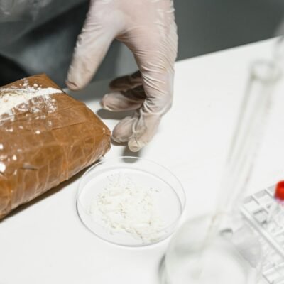 Close-up of a scientist's gloved hand with a powder sample in a laboratory setting.