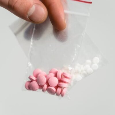 Hand holding a ziplock bag with pink and white pills on a white background.