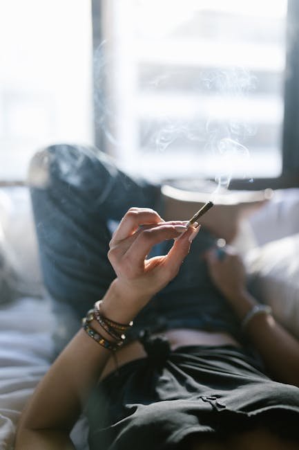 Woman lying on bed smoking a joint, enjoying a peaceful moment.