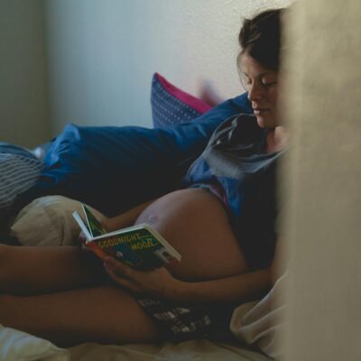 Pregnant woman reading on bed, enjoying a calm and intimate moment.